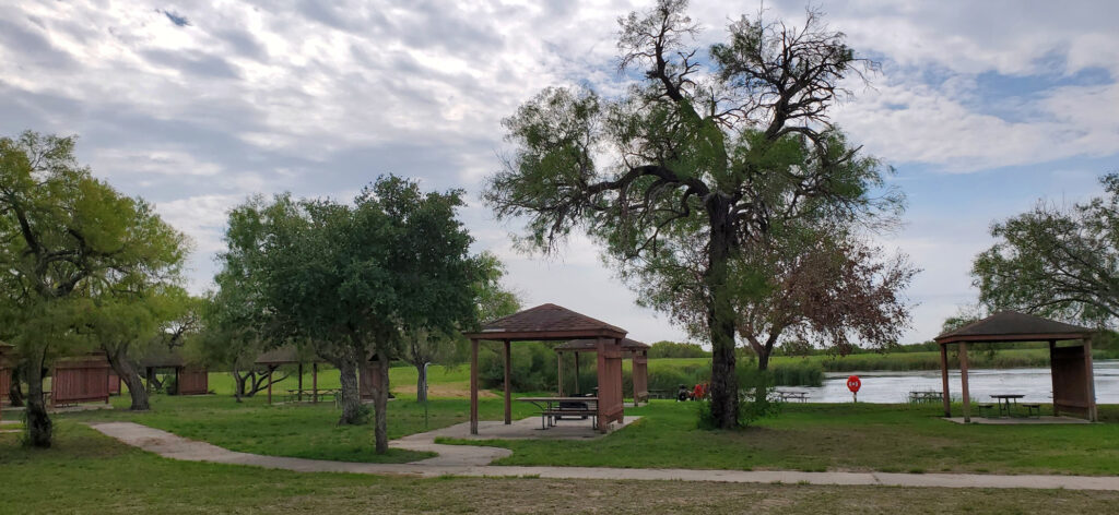 A covered picnic table in the park, with a small lake in the background.