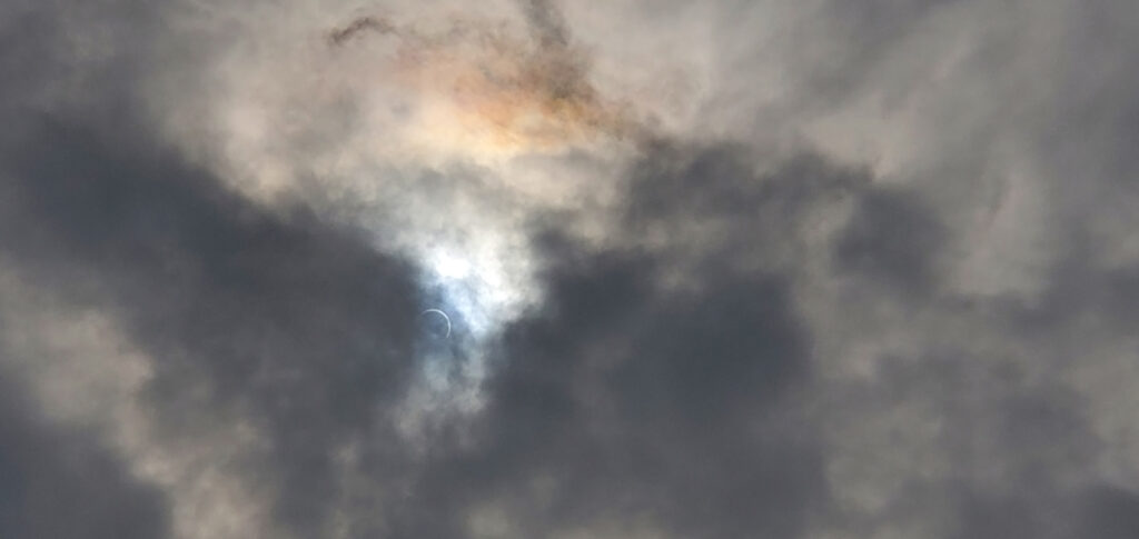 The eclipse at annularity as seen through the clouds with an unfiltered smartphone camera. The sunlight refracted off of the upper cloud deck, creating an iridescent effect.